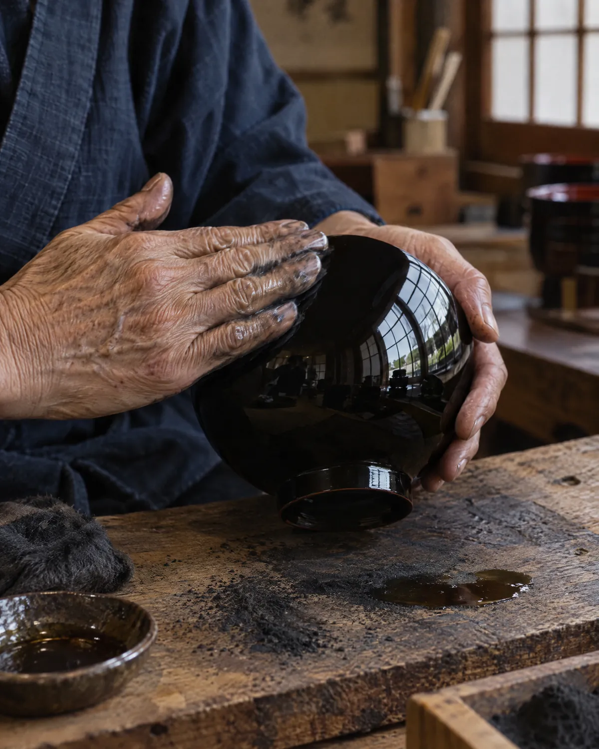 年配の職人の手が、黒い漆の器を手のひらで鏡のように磨いている
